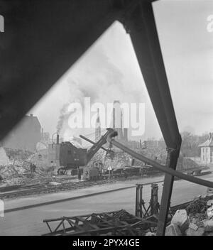 Foto non datata di un escavatore che scarica un mucchio di detriti e che carica carri con detriti da un blocco di appartamenti parzialmente bombardati vicino al Kurfuerstendamm nel quartiere di Charlottenburg a Berlino Ovest, una zona di occupazione britannica in quel momento. La macchina da costruzione diesel raccoglie mattoni e ghiaia con un dispositivo di presa. Una locomotiva idraulica diesel a scartamento ridotto tira i carri. Sullo sfondo, la torre (Hohler Zahn) della rovina della chiesa commemorativa Kaiser Wilhelm. Foto Stock