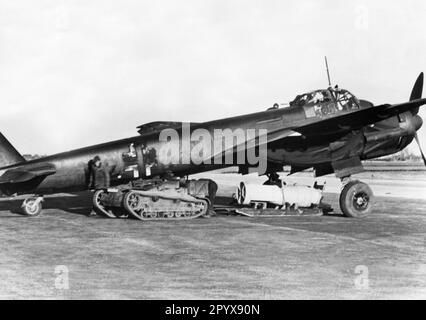 Un aereo da combattimento tedesco Junkers Ju 88 è carico di bombe per una missione contro obiettivi in Inghilterra. Il carro di un serbatoio francese funge da trattore. L'aereo è dipinto con una vernice camouflage scura, la croce del fascio è parzialmente di colore scuro pure. Foto: Rempel. [traduzione automatica] Foto Stock