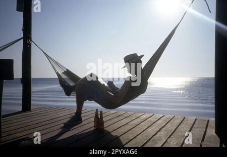 Data della foto: 13.03.1990 Un turista sull'isola di Rügen si rilassa leggendo nella sua amaca. [traduzione automatica] Foto Stock