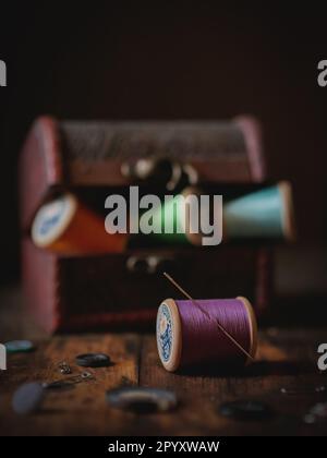 Fili da cucire multicolore su tavola di legno con fondo scuro Foto Stock