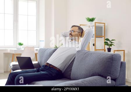 Felice uomo d'affari maturo seduto sul divano con un computer portatile e rilassarsi dopo una giornata di lavoro Foto Stock