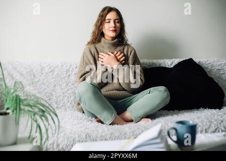 Tecniche di rilassamento: Donna che pratica il pranayama in posizione del loto sul letto, esercizi respiratori per ridurre lo sforzo e l'ansia, raggiungendo l'equilibrio interno Foto Stock
