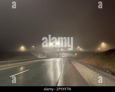 I lampioni si illuminano nella nebbia su un tratto di autostrada appannato. Foto Stock