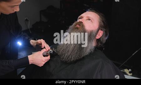 una ragazza parrucchiere taglia la barba di un uomo con un regolacapelli Foto Stock