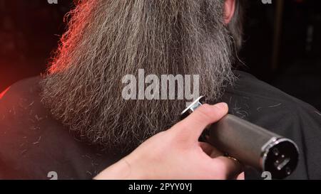 una ragazza parrucchiere taglia la barba di un uomo con un regolacapelli Foto Stock