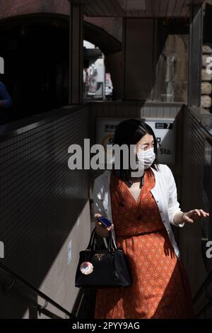 Una donna con una maschera facciale esce dalla stazione della metropolitana di Shinbashi a Tokyo. Foto Stock