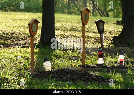 Tre tombe per animali domestici con lanterne, candele e pennarelli commemorativi in legno alla luce del sole serale Foto Stock