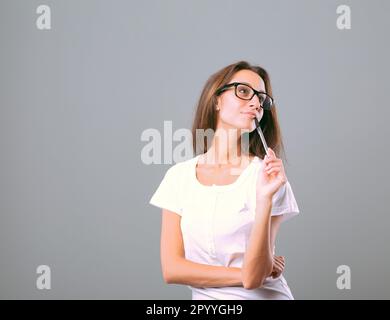 Ritratto di una giovane donna che vive un'emozione o una sensazione, pensando a qualcosa di affascinante o piacevole, tenendo una penna in bocca, indossando Foto Stock