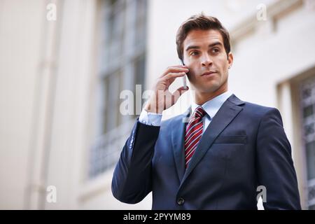Comunicazioni urbane. Un bel uomo d'affari in tuta che parla sul suo cellulare in un ambiente urbano. Foto Stock