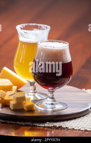 Bicchieri di birra belga bionda gialla e bruna scura realizzati in abbazia e legno con varietà di formaggi belgi, abbinamenti di cibo e birra in Belgio Foto Stock