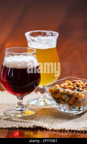 Bicchieri di birra belga bionda gialla e bruna scura preparati in abbazia serviti al bar con noci da festa, primo piano Foto Stock