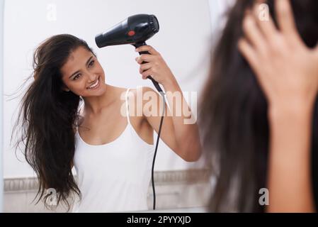 Mettendo insieme la sua acconciatura. Una giovane donna che asciuga i capelli. Foto Stock