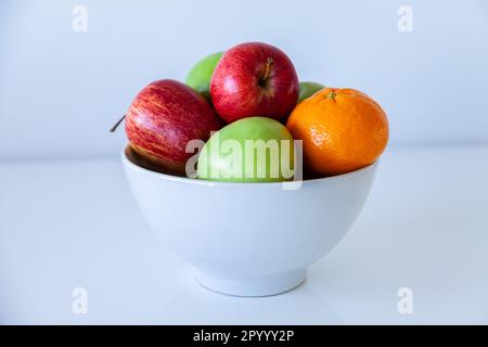 Mele rosse e verdi e un mandarino in un cestino di frutta su bianco Foto Stock