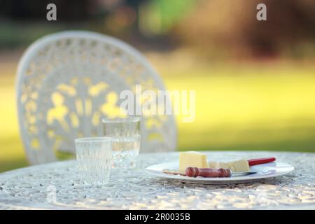 Bicchieri con acqua e piatto di formaggi con coltelli su un tavolo vintage all'aperto Foto Stock