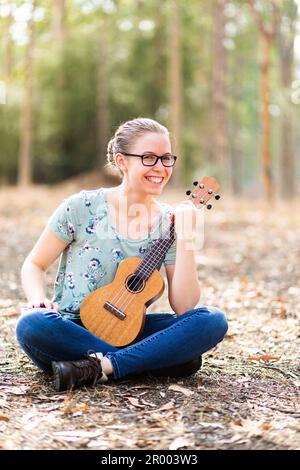 Giovane musicista con ukulele che suona lo strumento nel paddock asciutto in Australia Foto Stock