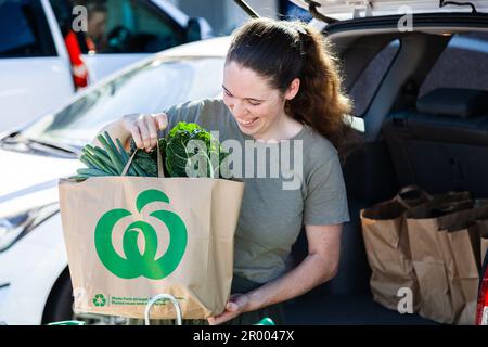 Una giovane donna sorridente con Click and Collect direttamente per mettere le drogherie di Woolworths che le caricano nella sua auto Foto Stock