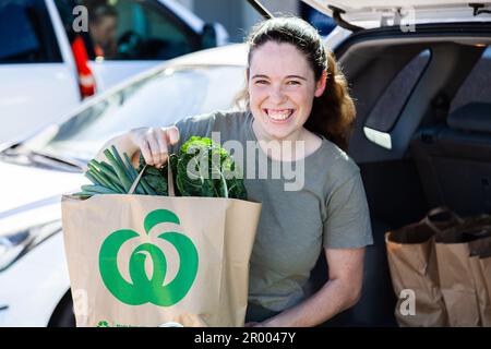 Una giovane donna sorridente con Click and Collect direttamente per mettere le drogherie di Woolworths che le caricano nella sua auto Foto Stock