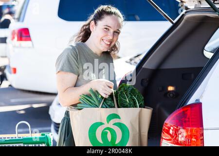 Una giovane donna sorridente con Click and Collect direttamente per mettere le drogherie di Woolworths che le caricano nella sua auto Foto Stock