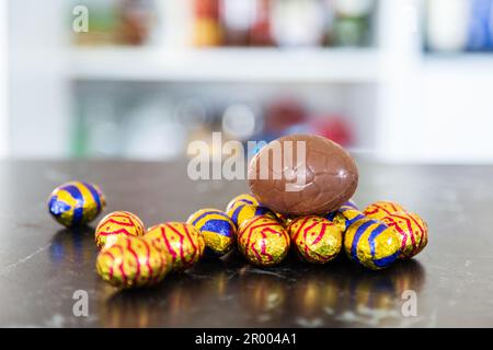 Uova di Pasqua su panca con cioccolato e dolcetti avvolti in fogli di alluminio Foto Stock