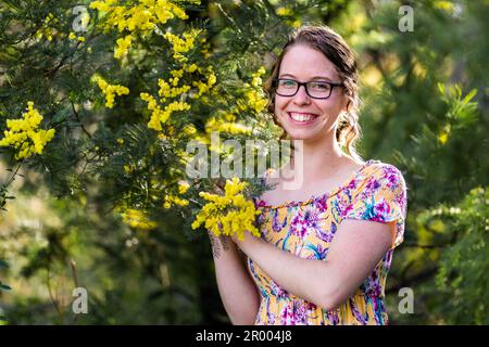 Giovane e felice adolescente australiano in piedi accanto a un cespuglio d'oro in fiore Foto Stock