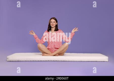 Giovane donna meditando su morbido materasso su sfondo viola chiaro Foto Stock