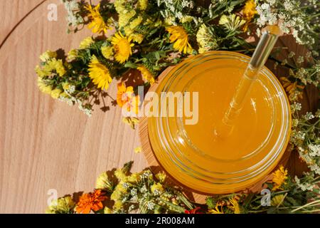 Delizioso miele fresco in vaso di vetro e bellissimi fiori su tavolo di legno, piatto Foto Stock