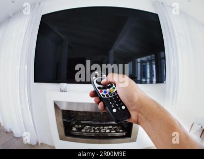 POV, televisione e mani dell'uomo con telecomando in un soggiorno per rilassarsi, weekend e film. Canale, cambio e maschio in una sala guardando la tv Foto Stock