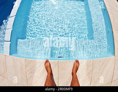 Acqua, piedi e sopra l'uomo nuotatore in una piscina per l'allenamento, relax e divertimento estivo durante le vacanze. Vista dall'alto, a piedi nudi e atletico maschio in piedi presso la Foto Stock