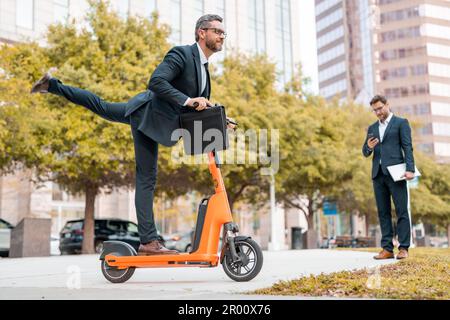 Business pazzo, veloce e facile. Divertente uomo d'affari eccitato in un vestito a cavallo di uno scooter in una riunione d'affari. Uomo d'affari in sella a uno scooter elettrico Foto Stock