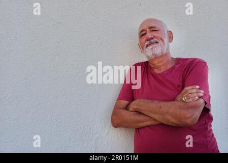 Un uomo anziano maturo che indossa una camicia rosa e che si erge contro una parete bianca con spazio per il copyspace Foto Stock