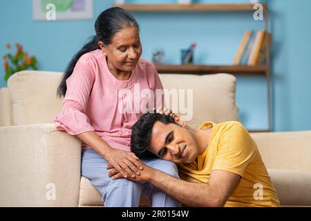 Madri anziane indiane che parlano con il figlio adulto consolando mentre il figlio dorme sul giro delle madri nel paese - concetto di maternità, supporto parentale e. Foto Stock