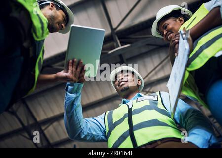 Meno documenti, più risultati. Inquadratura ad angolo basso di un gruppo di costruttori che utilizza un tablet digitale mentre lavora in cantiere. Foto Stock