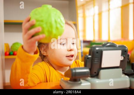 bambino in asilo, sala giochi, giocare con i giocattoli, imparare. Giochi in negozio, verdure e frutta, registratore di cassa e bilance. Foto Stock