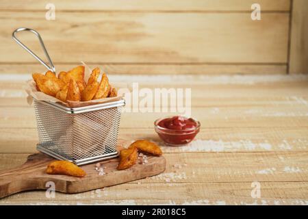 Patatine fritte in metallo cestello con sale e ketchup su vecchio legno chiaro sfondo clous up. Patate fritte. Concetto di fast food e cibo malsano. Foto Stock