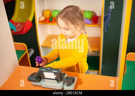 bambino in asilo, sala giochi, giocare con i giocattoli, imparare. Giochi in negozio, verdure e frutta, registratore di cassa e bilance. Colorato Foto Stock