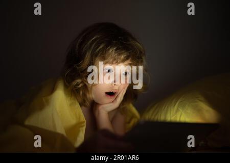 Bambino che guarda il tablet prima di dormire. Il bambino legge l'e-book. Il ragazzino guarda lo schermo del tablet in alto. Ragazzo che gioca un tablet sdraiato su un Foto Stock