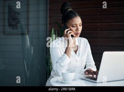 Una donna d'affari multitasking è potente. una giovane e attraente donna d'affari seduta in ufficio e che usa il suo laptop mentre parla sul suo cellulare. Foto Stock