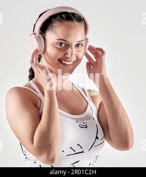 La musica mi fa muovere immediatamente. Ritratto da studio di una giovane donna sportiva che indossa le cuffie su sfondo bianco. Foto Stock