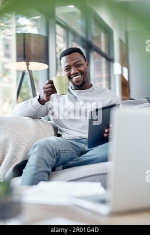 Ive ha tutto quello che mi serve per sentirmi bene proprio qui. un giovane uomo che usa un tablet digitale e che ha un caffè sul divano a casa. Foto Stock