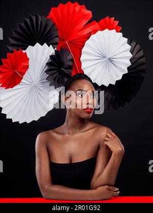 Prendendo in prestito alcune tendenze di bellezza da attraverso lo stagno. Studio shot di una bella giovane donna in posa con un tifoso origami su uno sfondo nero. Foto Stock