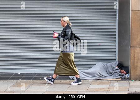 Donna in gonna verde lungo passando senza casa uomo sdraiato in porta Preston, Lancashire UK. Maggio 2023. Negozi e negozi nella strada principale del centro di Preston il giorno dell'incoronazione del Re. Credit; MediaWorldImages/ AlamyLiveNews Foto Stock