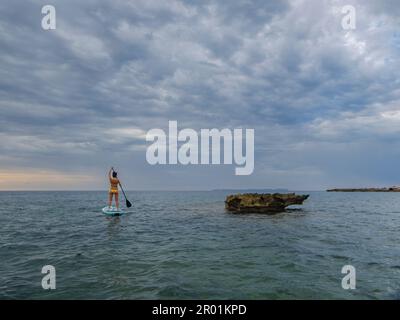 Donna in tavola da surf sotto un cielo drammatico, Estalella, costa di Llucmajor, Maiorca, Isole Baleari, Spagna. Foto Stock