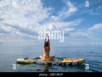 Donna che pratica yoga su una tavola da surf sotto un cielo drammatico, Estalella, costa di Llucmajor, Maiorca, Isole Baleari, Spagna. Foto Stock