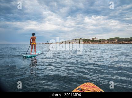 Donna in tavola da surf sotto un cielo drammatico, Estalella, costa di Llucmajor, Maiorca, Isole Baleari, Spagna. Foto Stock