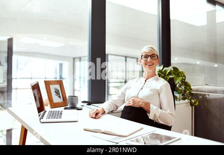 Shes un go-getter, ora per diventare un mom anche. Ritratto di una donna d'affari incinta seduta su una scrivania in un ufficio. Foto Stock