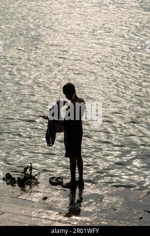 Un uomo che fa un bagno durante il tramonto al ghat del fiume santo Ganga nel nord di Kolkata. Foto Stock