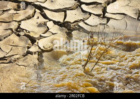 Acque infurianti e torbidi dopo diversi giorni di pioggia contro terra infertile bruciata dal sole - immagine concettuale Foto Stock