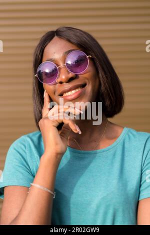 Catturare l'essenza dell'estate: Un ritratto di un giovane turista afro-americano in una T-shirt verde e le sfumature contro una parete marrone Foto Stock