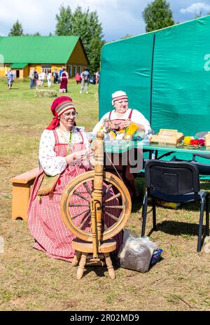 Lubytino, Russia - 16 luglio 2022: Donna in abiti nazionali russi che mostra la tradizionale lana che gira su una vecchia ruota di legno durante il suo Foto Stock