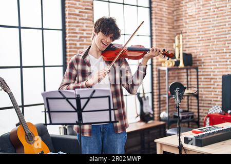 Giovane musicista ispanico sorridente sicuro di suonare il violino in studio musicale Foto Stock